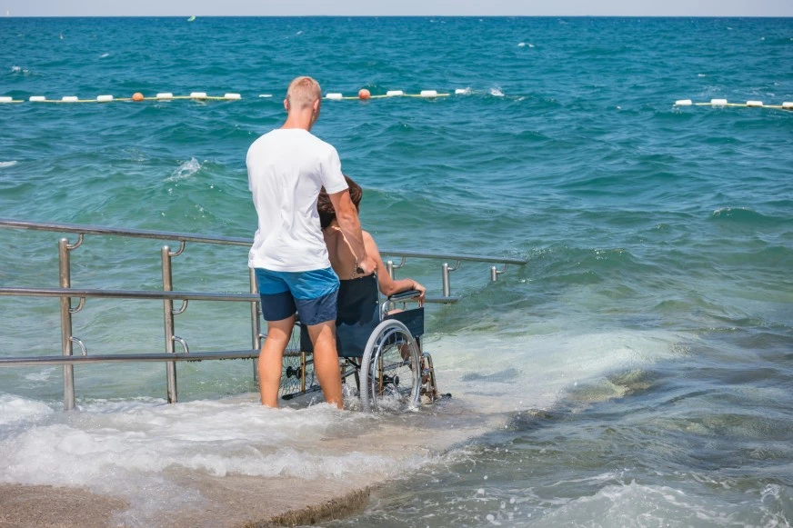 Carer with disabled woman in wheelchair going into ocean